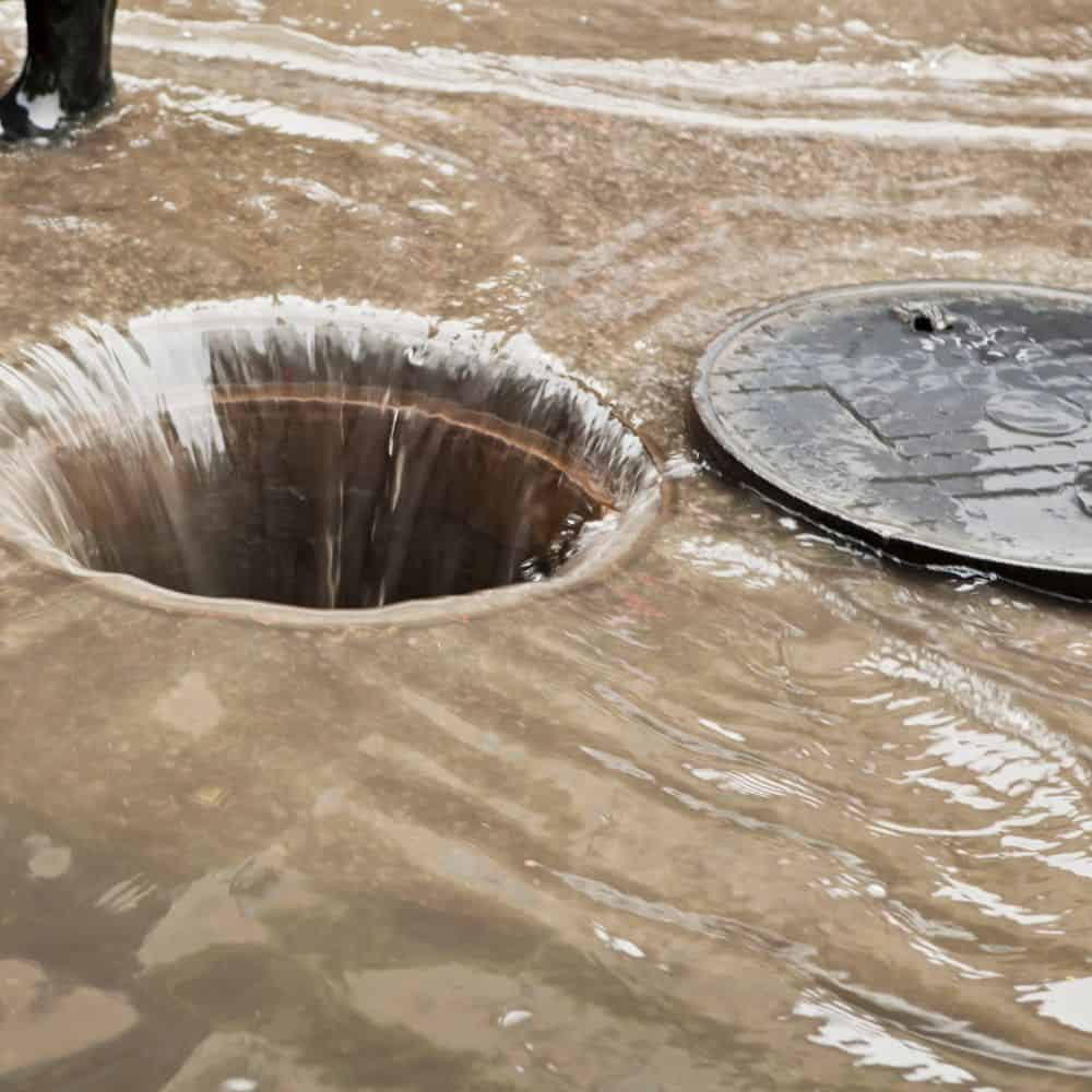Flooded drain cover with water overflow, drainage repair service.